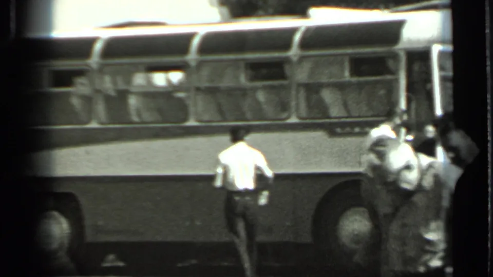 Black-and-white 8mm frame from Russia in 1963 showing several men near a stopped vintage bus, with faces distant and indistinct.