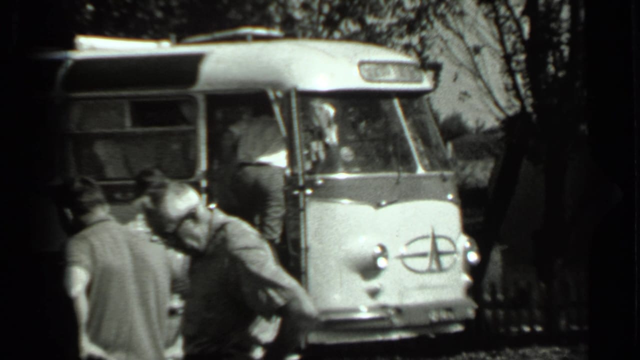1963 Russia 8mm frame of men near the front of a Soviet-era bus, including a visible emblem on the vehicle nose.