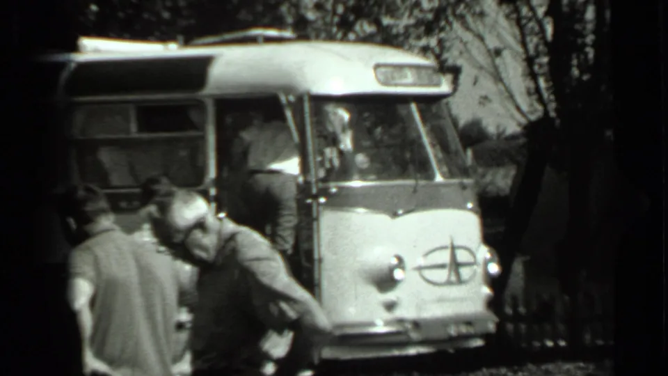 1963 Russia 8mm frame of men near the front of a Soviet-era bus, including a visible emblem on the vehicle nose.