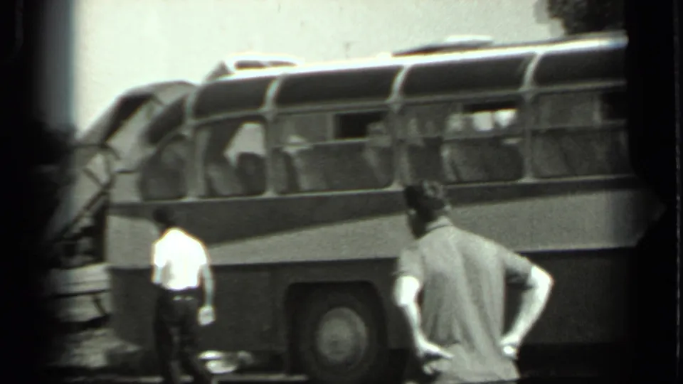 1963 Russia 8mm frame showing the side of a Soviet-era bus with adult men nearby and trees in the background.