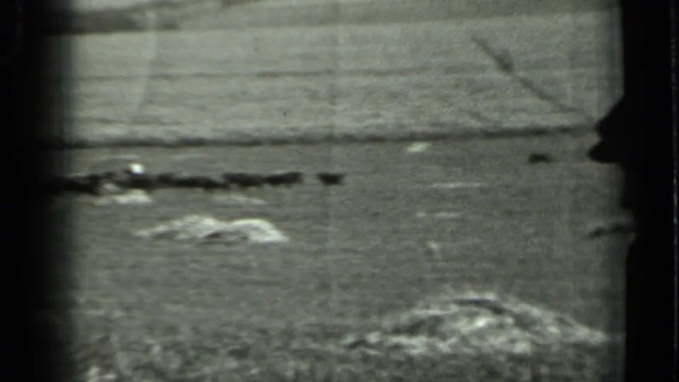 1963 Russia home-movie frame showing an open rural field, low rocks, distant horizon, and a dark horizontal line in the middle distance.