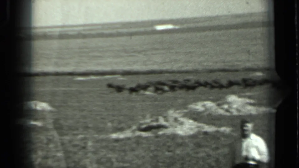 1963 Russia home-movie frame with a man near the lower right edge, rocks in the field, and a distant horizon under a bright sky.