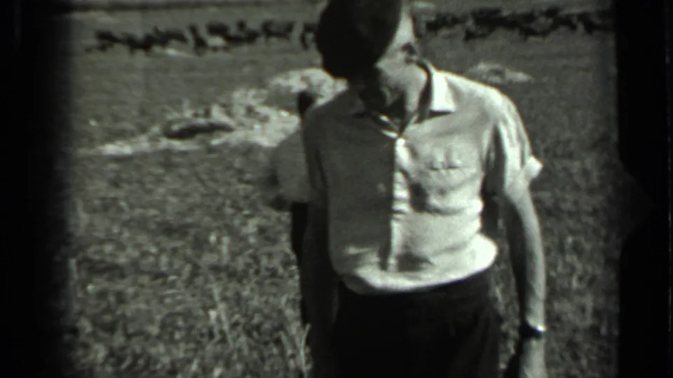 Closer black-and-white frame of the man facing the camera, wearing a light short-sleeved shirt in the field.