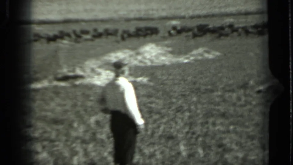 1963 Russia 8mm frame showing a distant man in a light shirt and dark trousers walking through an open field.