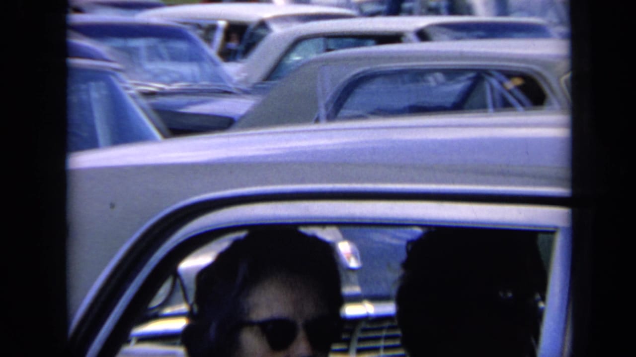 Light-colored sedan with a person wearing sunglasses visible through the side window.
