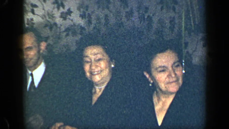 A man in a suit and tie appears beside two smiling women in a dim 1948 New York interior home-movie frame.