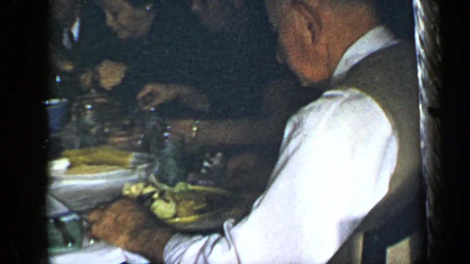 1948 New York dinner scene with a waiter in a white shirt and dark vest serving food near seated guests.