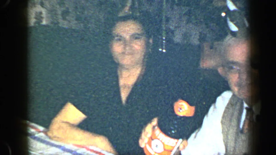 1948 New York home-movie frame of a woman and older man seated close together at an indoor celebration table.
