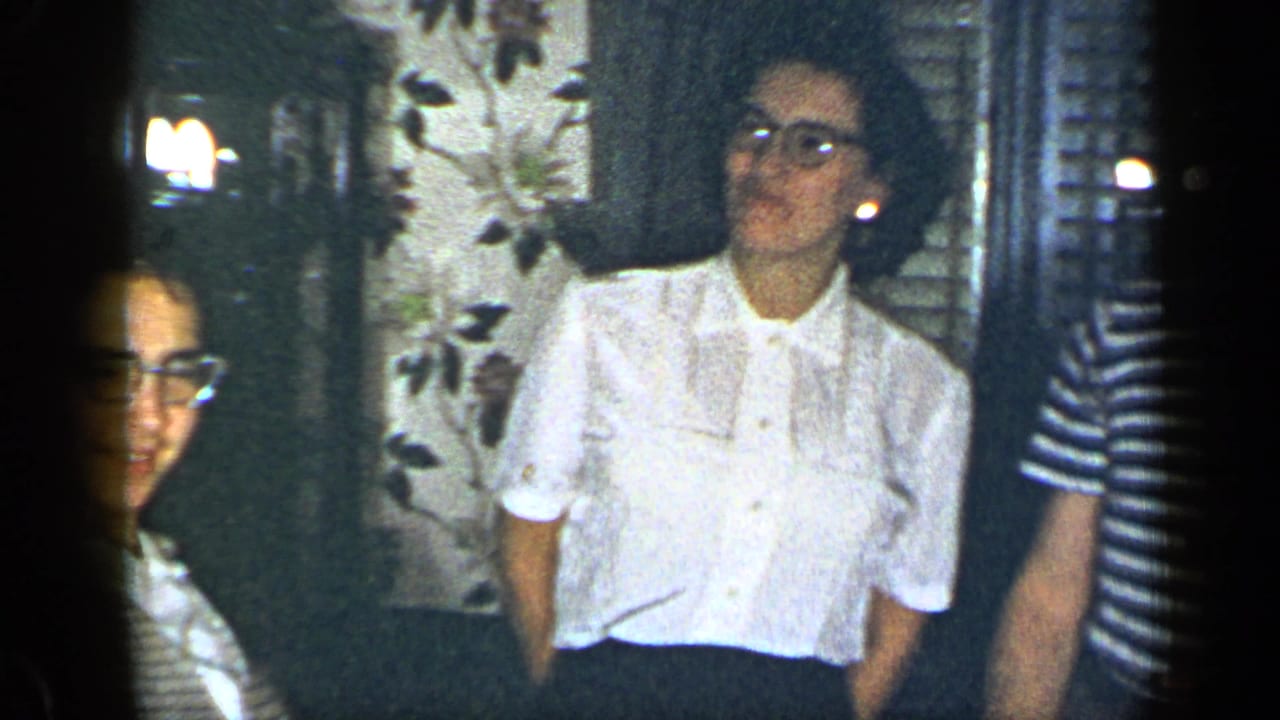 Adults standing indoors near floral wallpaper and shutters during a party.