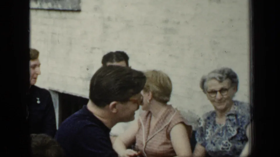 1948 New York home-movie frame showing a man in glasses leaning toward a woman in a sleeveless dress as another woman looks on.