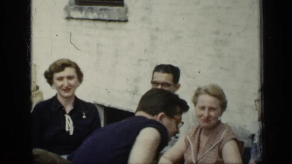 1948 New York outdoor social scene with seated adults, a man bending forward, and two women facing the camera near a pale wall.