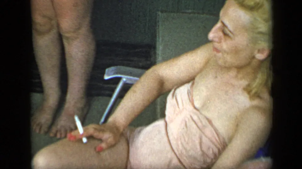 1948 New York frame of a blonde woman in a pale pink towel seated outdoors with a cigarette in hand.