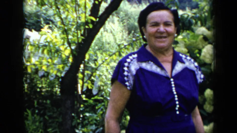 In this 1948 New York frame, the woman smiles toward the camera while standing or walking near pale flowering shrubs and dense greenery.