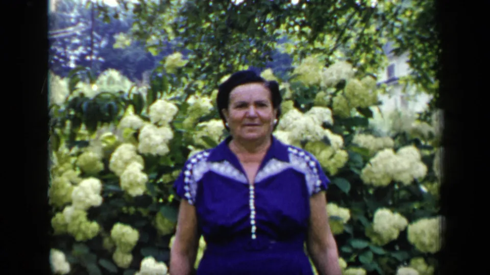 Adult woman in a purple dress with white trim faces the camera in a New York garden, consistent with 1948 home-movie metadata.