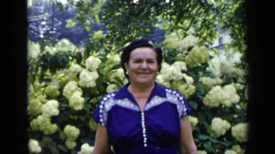 The same adult woman smiles toward the camera in a flowered garden, matching the supplied 1948 New York home-movie context.
