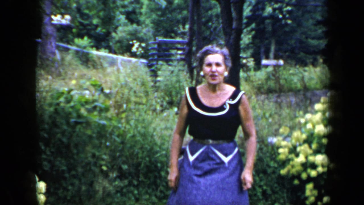 Woman standing in a garden with trees and foliage behind her.