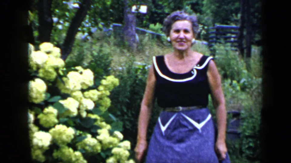 A closer 1948 New York garden view shows the woman near yellow hydrangeas, facing the camera in a black top and purple skirt.