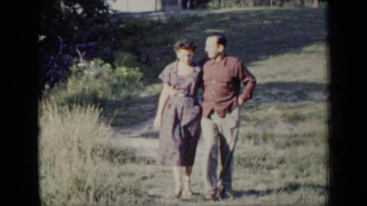 In 1948 New York home-movie footage, an adult woman in a plaid dress and a man in a dark shirt walk together on grass.