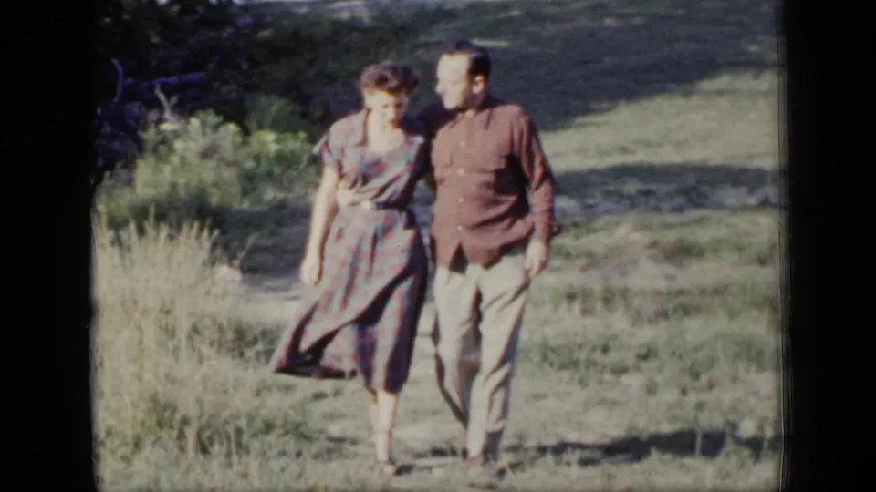The couple continues across the lawn, with the woman in a patterned dress and the man in light trousers beside her.