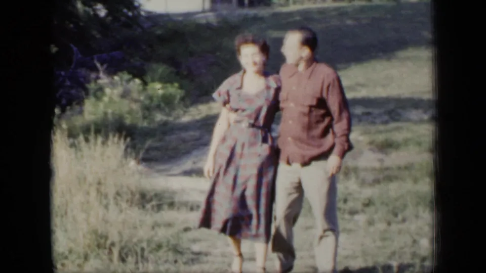 The 1948 home-movie frame shows the couple nearer the camera, walking together in a bright grassy setting.