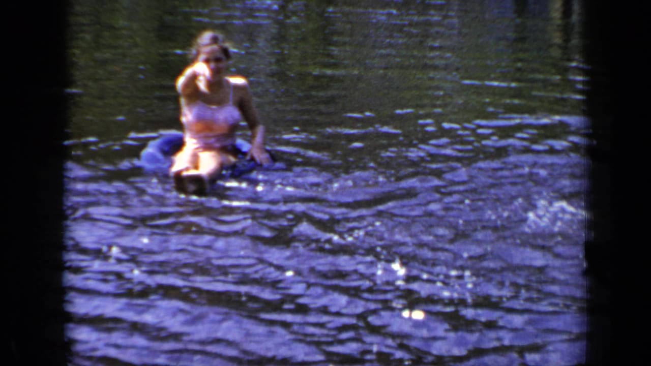Swimmer sitting on a blue inner tube in dark rippling water.