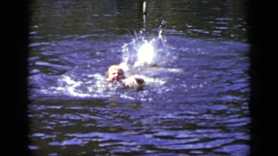 1948 New York home-movie frame showing the swimmer close to the surface while bright splashes and ripples spread behind them.
