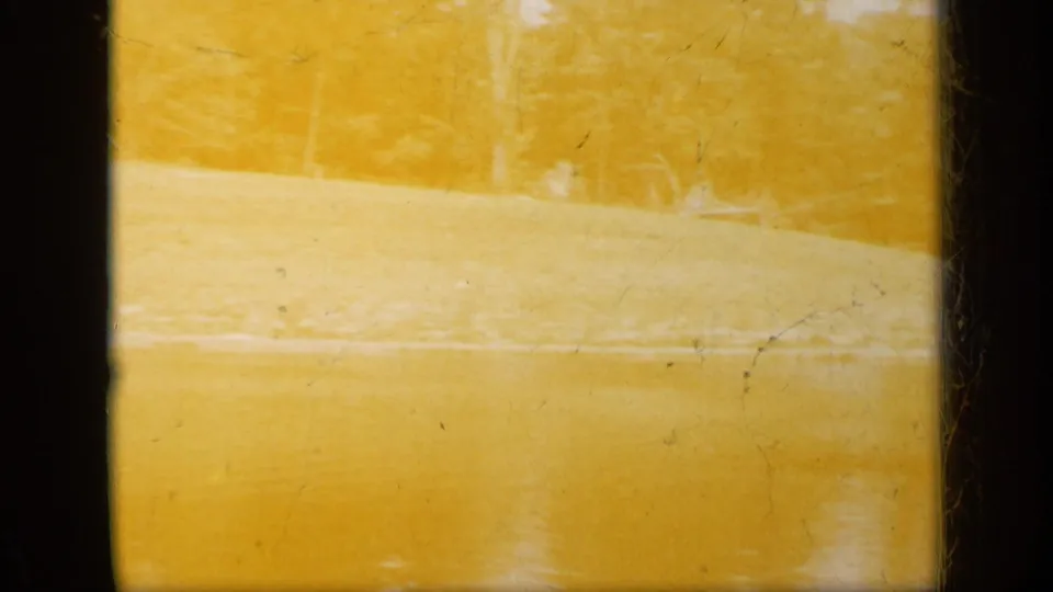 End frame from the 1948 8mm clip showing yellowed film texture, faint shoreline forms, scratches, and soft exposure variation.