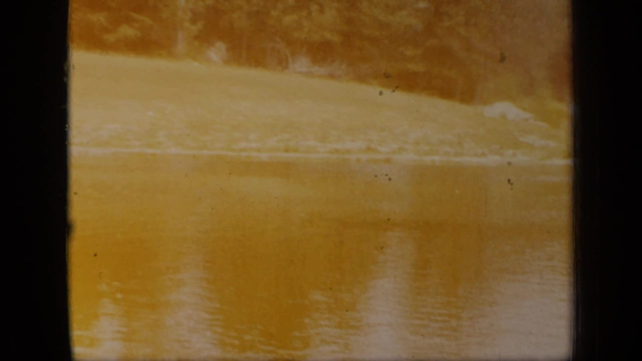 1948 New York 8mm frame with yellow-tinted lake water, a distant shoreline, soft focus, grain, and visible film-frame edges.