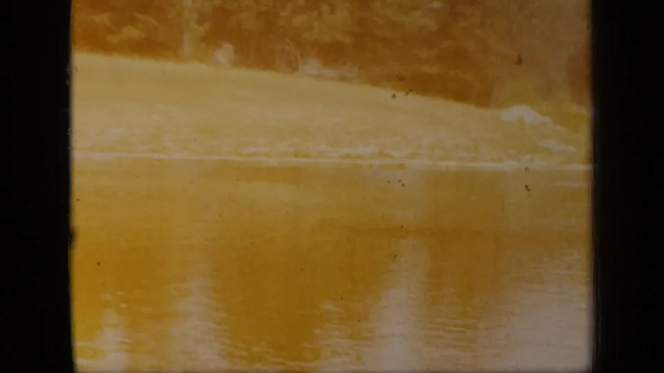 1948 New York 8mm frame with yellow-tinted lake water, a distant shoreline, soft focus, grain, and visible film-frame edges.