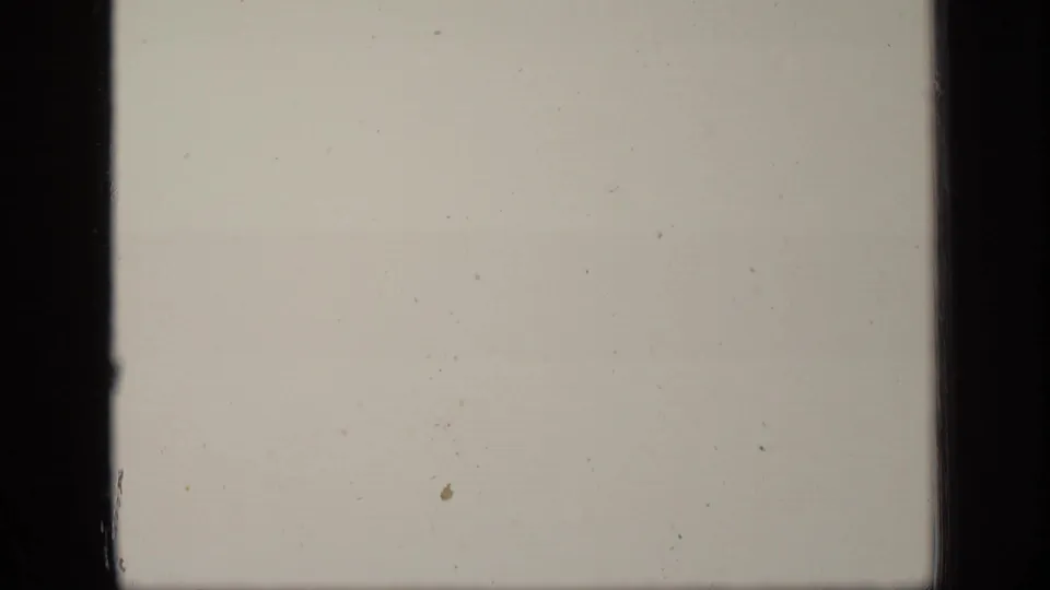 Pale overexposed or blank 8mm frame with dust specks, subtle discoloration, and dark vertical film borders.