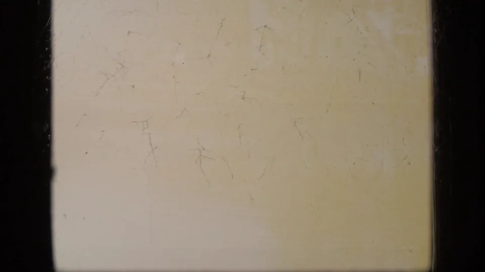 Yellowed 8mm frame with scratches, faint staining, dust, and dark film borders, with no clear subject visible.
