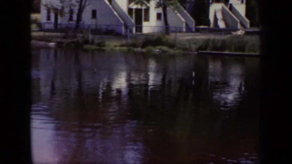 1948 New York 8mm view of lakeside houses, railings, lawn, and dark water reflections along a quiet shoreline.
