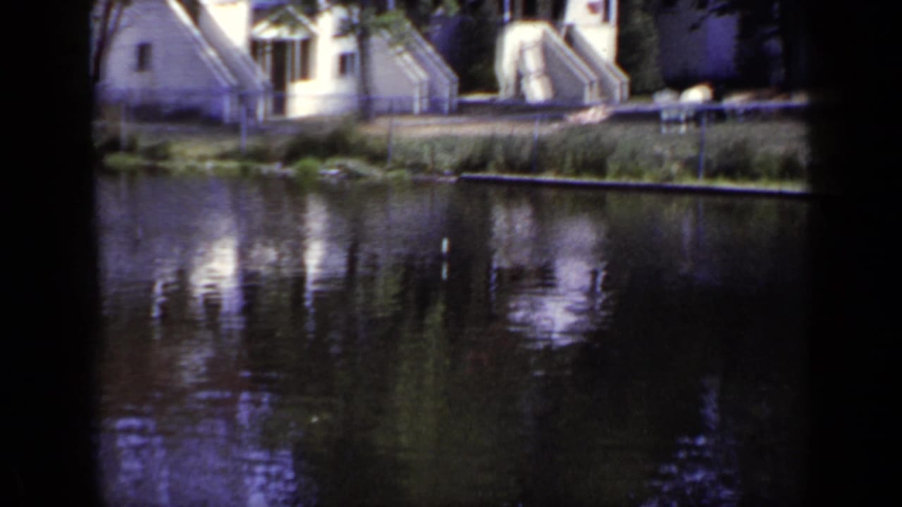 Pond water reflecting small houses and trees, with dark 8mm frame edges.