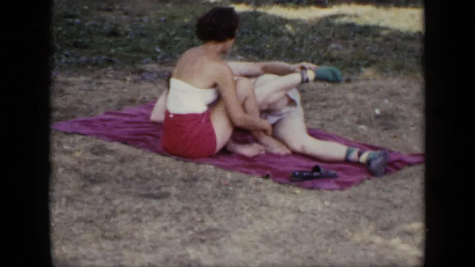 The same adult couple appears seated on a red blanket outdoors, with casual swimwear and shoes visible on the grass.