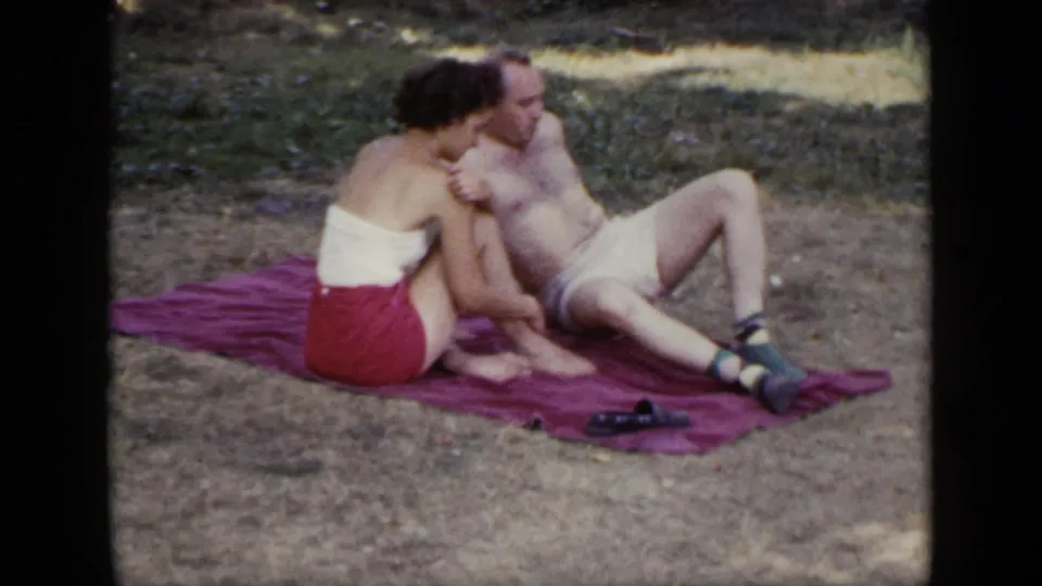 An adult woman in a white top and red skirt or shorts leans close to a reclining man on a red blanket in 1948 New York footage.