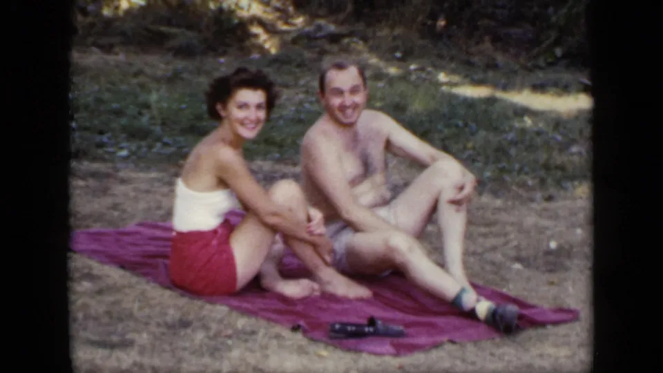 The woman and man smile toward the camera from a purple blanket in metadata-supported 1948 New York home-movie footage.