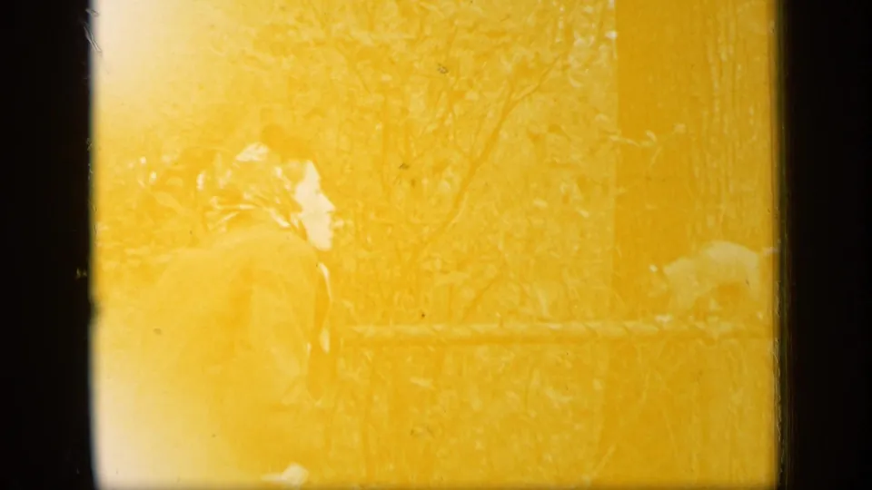 A yellow-tinted 1948 New York frame shows a woman bending near a fence, with a squirrel faintly visible at the right.