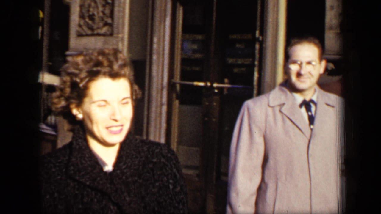 Woman in a dark coat faces the camera near a city building entrance.