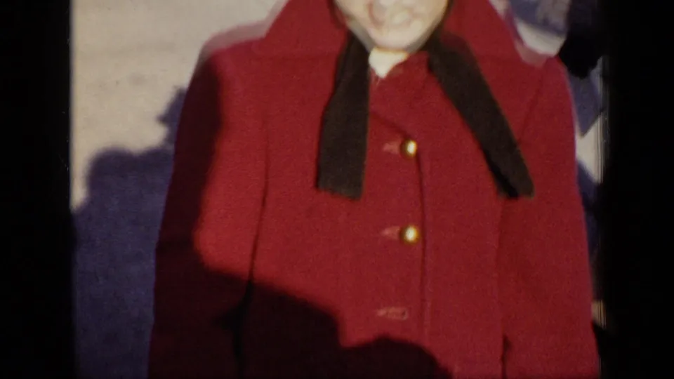 A woman in a red coat with a dark collar is framed close to the camera in 1948 New York home-movie footage.