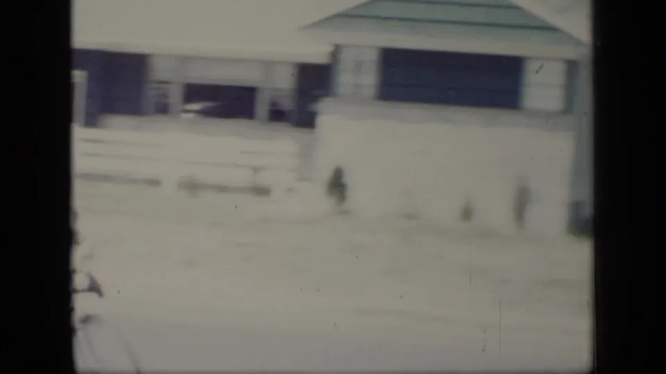 The bicycle riders partly leave the frame, leaving a soft view of the residential house, fence, and bright street area in 1948 New York footage.