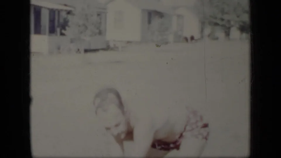 In 1948 New York home-movie footage, a smiling man bends in a sunlit yard, partly washed out by exposure.