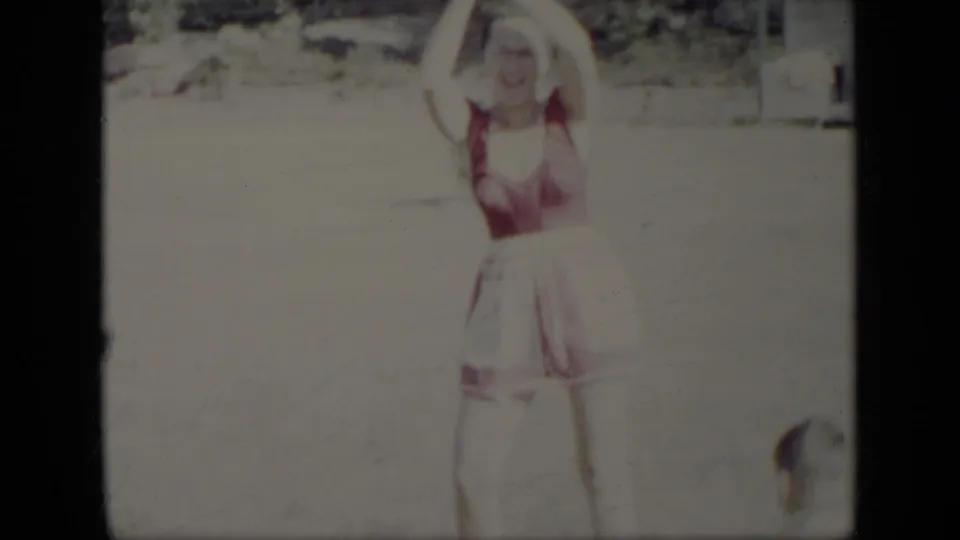 In this 1948 New York home-movie frame, a woman in a red-and-white swimsuit stands in a sunny yard with her arms raised.