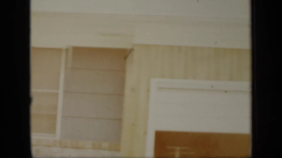1948 New York home-movie frame showing a wood-sided house exterior, window, and partial garage opening in soft 8mm color.