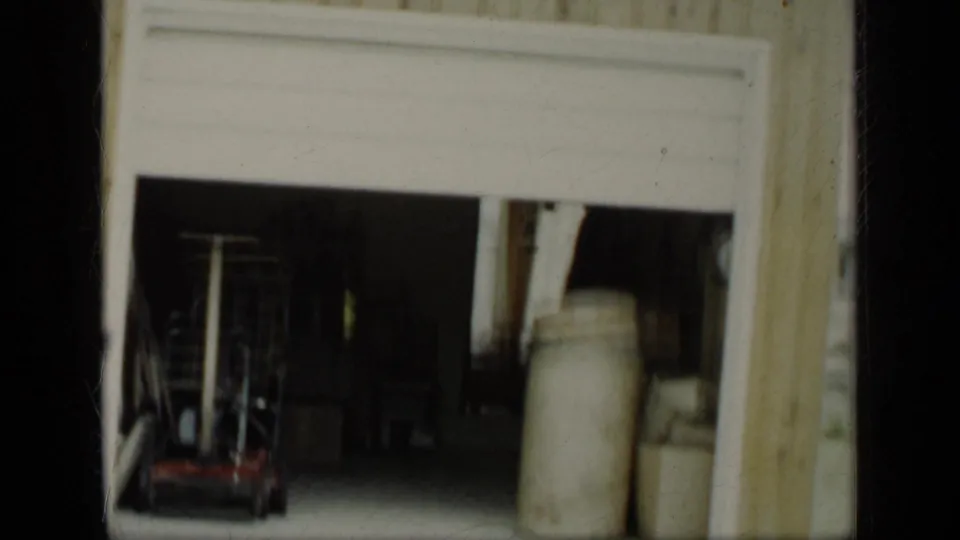 Open residential garage in New York, 1948, with dim storage space, equipment, and large containers visible from outside.