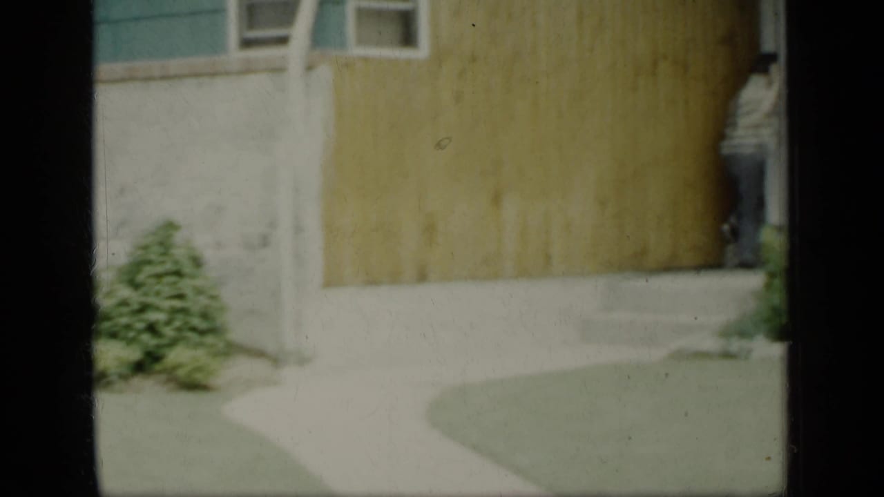 House exterior with concrete walkway, lawn, green trim, and a man partly visible at the doorway.