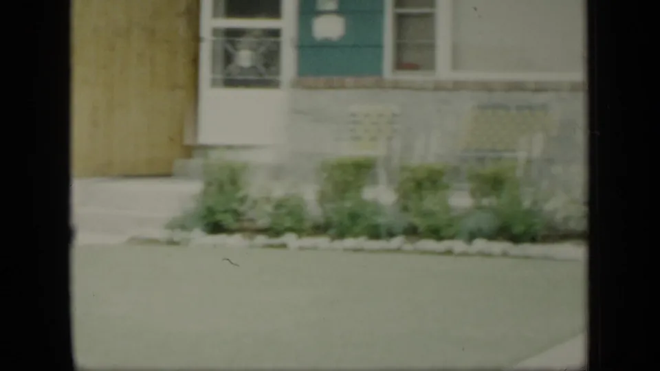 1948 New York home-movie frame showing the side of a house, lawn, shrubs, windows, and stone foundation detail.