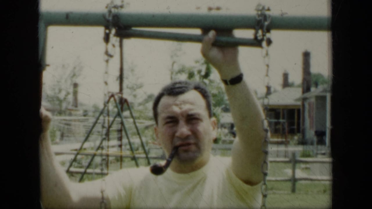Man with a pipe grips a swing set bar in a backyard.