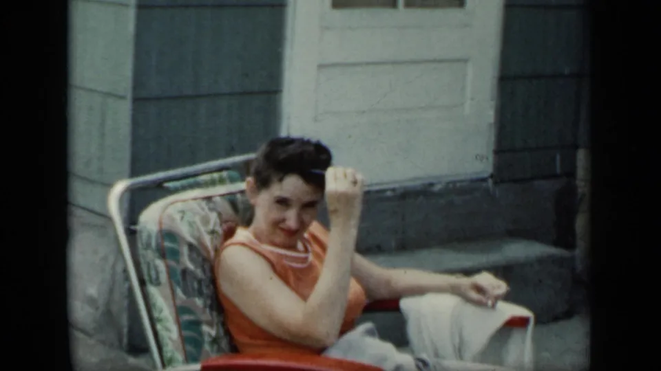 1948 New York home-movie frame of a woman in an orange top looking toward the camera as she lowers sunglasses.
