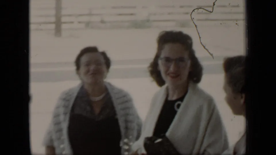 1948 New York home-movie frame showing women in mid-century dress at an outdoor reception, with smiles and casual conversation.