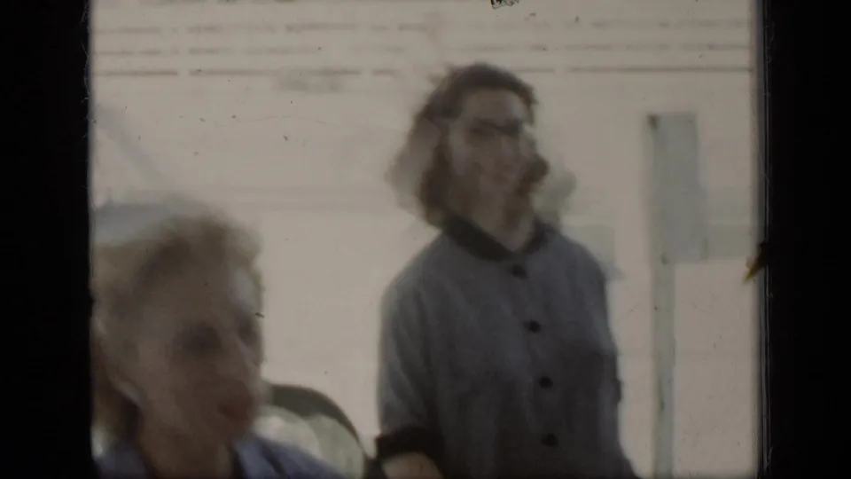A woman in glasses appears beside another adult in soft-focus 1948 New York street footage, with parked cars behind them.